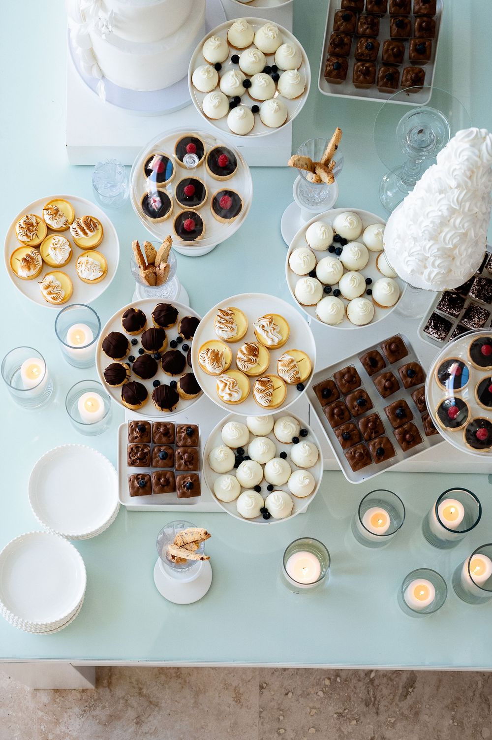 Overhead view of an elegant dessert spread featuring chocolate truffles, macarons, and tea lights on a light blue surface.