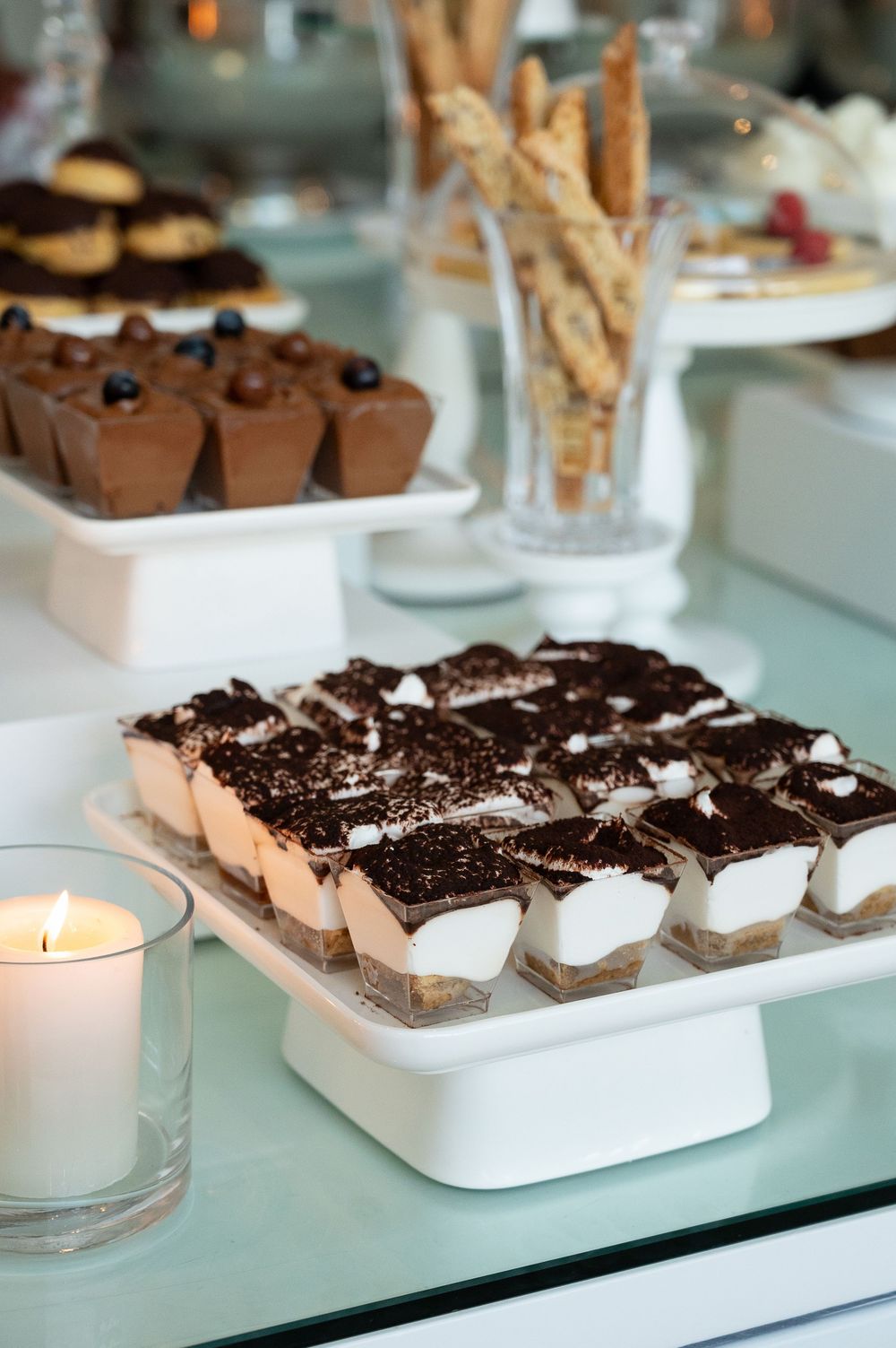 Chocolate dessert squares topped with crumbled Oreo cookies arranged in white serving dishes on a glass surface with tea lights.