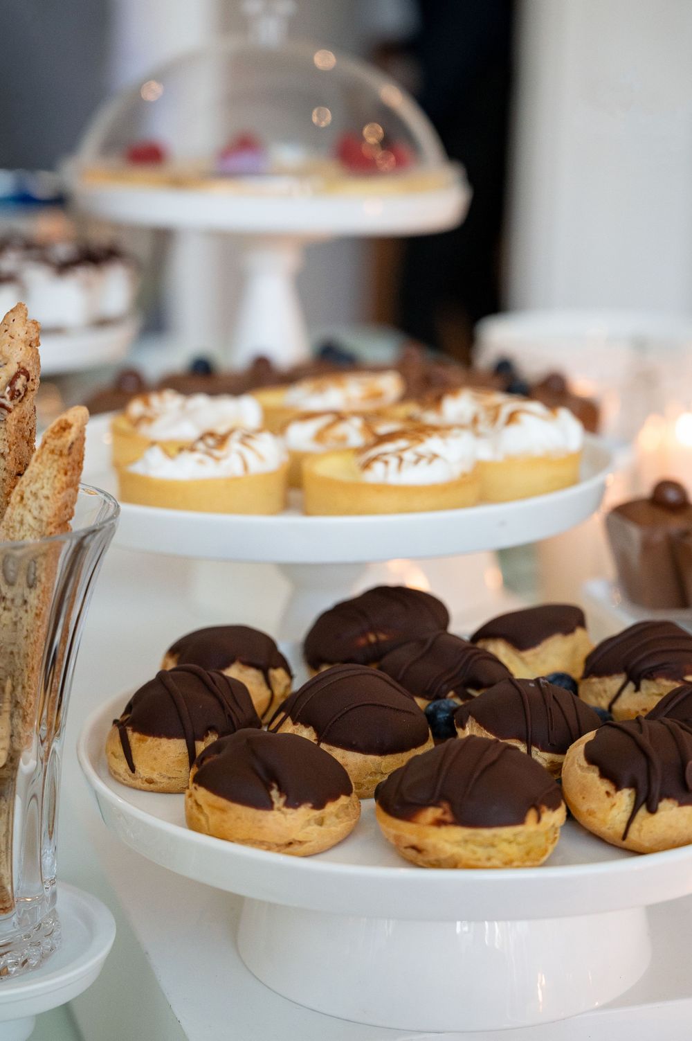 Chocolate-dipped cream puffs and pastries displayed on elegant white tiered serving stands at a dessert table.
