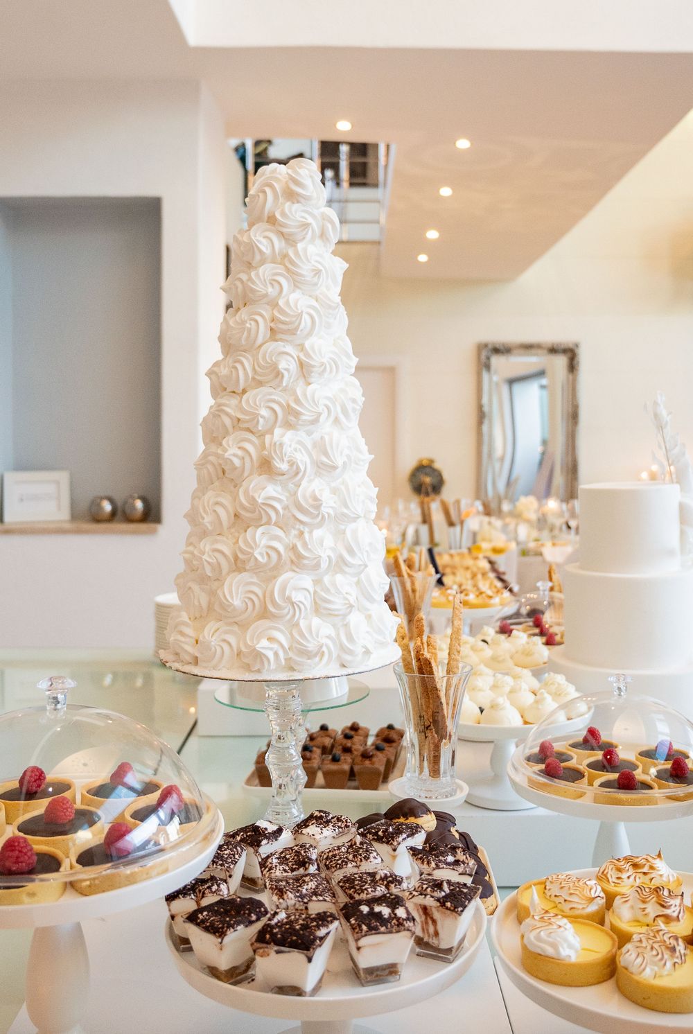 Elegant white wedding cake and delicious dessert display featuring cookies and pastries on a buffet table.