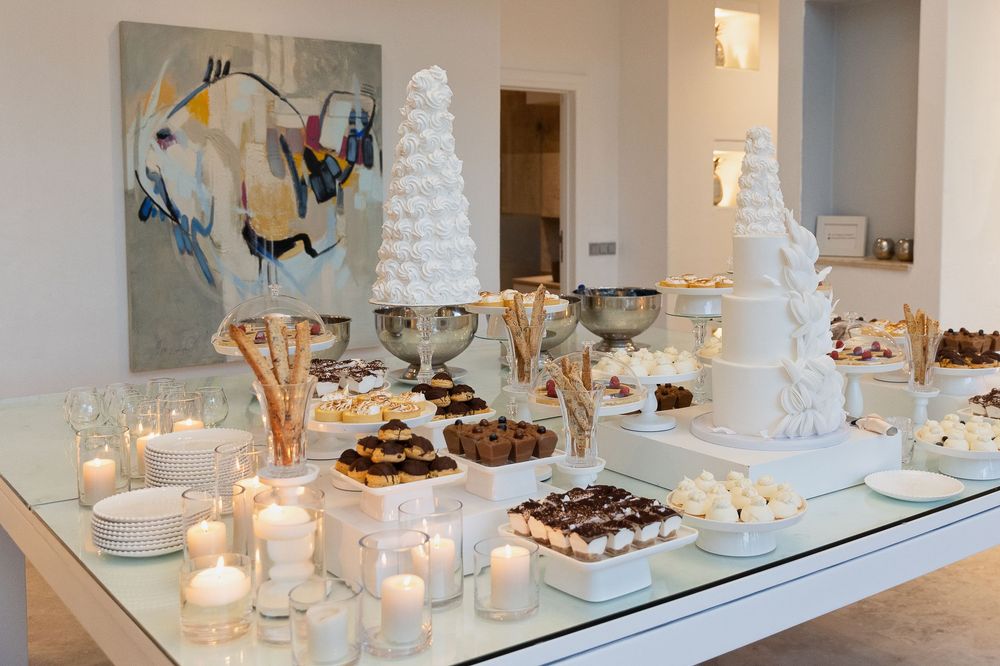 Modern white dessert buffet featuring multiple cakes and pastries illuminated on glass shelves with soft lighting.