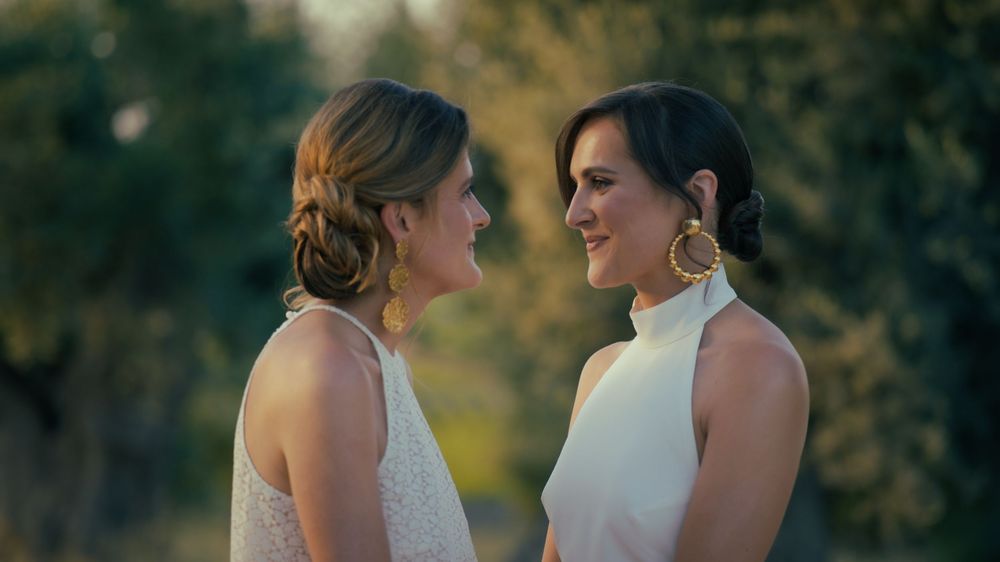 Two people in formal wear having an intimate conversation outdoors with blurred natural background.