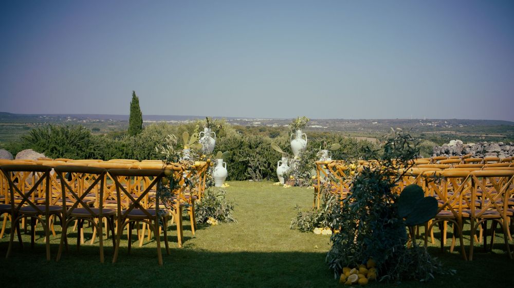 Expansive outdoor wedding ceremony setup with wooden cross-back chairs arranged in rows facing a scenic mountain landscape.