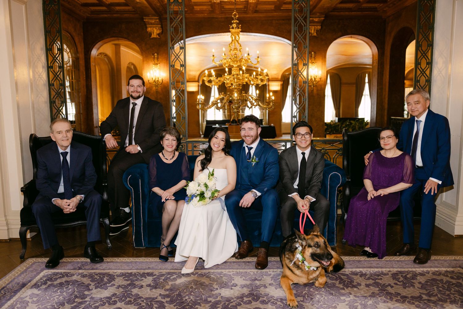 Small intimate wedding ceremony in an elegant indoor venue with guests seated on gold chairs under a crystal chandelier.