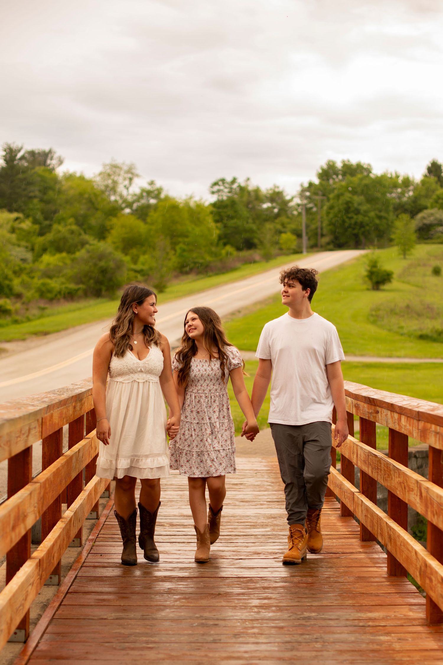 Three friends walking and laughing together on a wooden bridge boardwalk surrounded by green nature.
