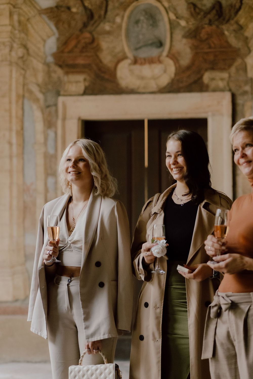 A group of stylish guests in neutral toned outfits holding champagne glasses at an elegant venue.