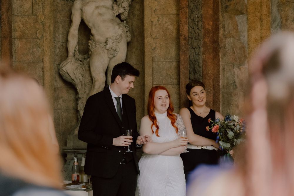 Wedding party members celebrate during reception in historic stone venue with rustic backdrop and decorative lighting.