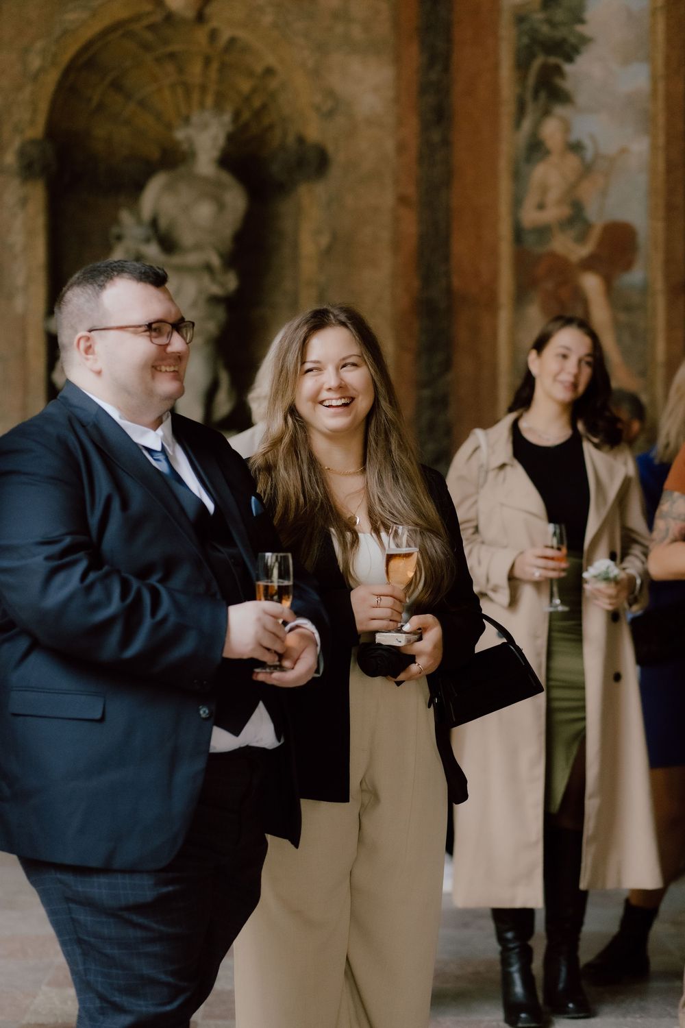 Wedding guests mingling and laughing in a historic colonnade with stone archways.