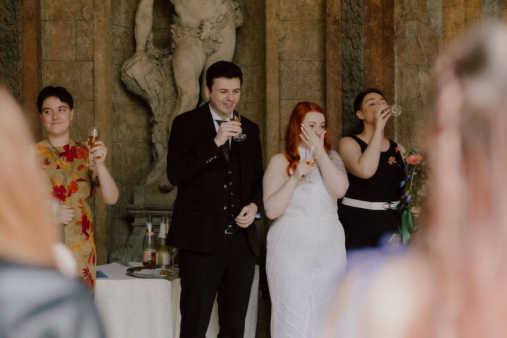 Dancing couples celebrate at an elegant wedding reception with red floral decorations in an ornate indoor venue.