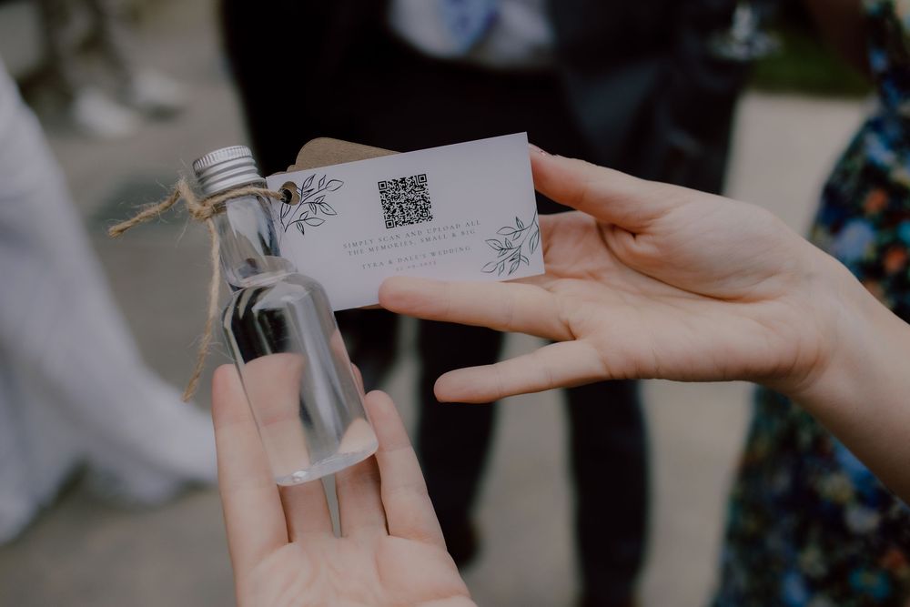 Hands holding a small glass bottle with an attached tag at an event.