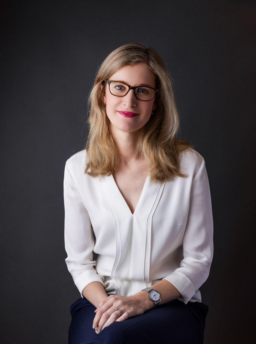 Professional portrait of woman in white blouse and glasses against dark background.