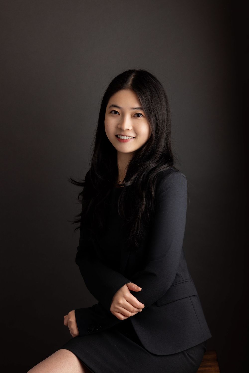 Professional portrait against dark background with black blazer and warm smile.