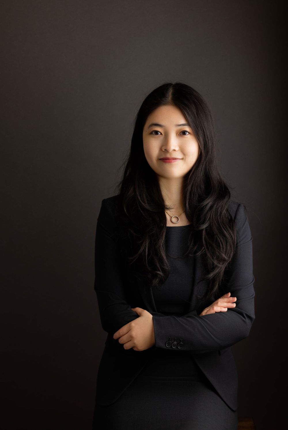 Studio portrait of person in black business attire against dark backdrop.