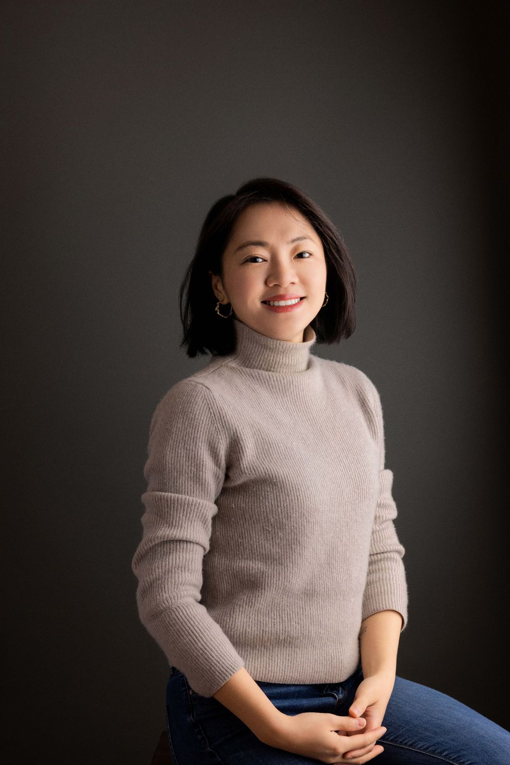 Portrait featuring beige turtleneck sweater against dark studio background.