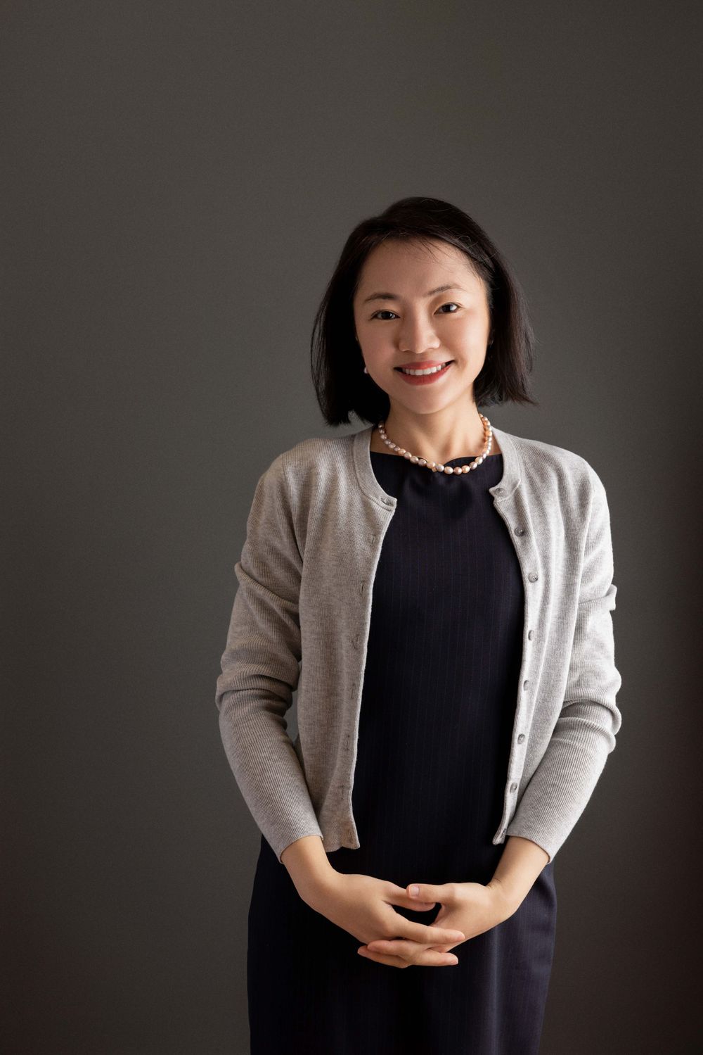 Professional headshot wearing grey cardigan and pearl necklace.