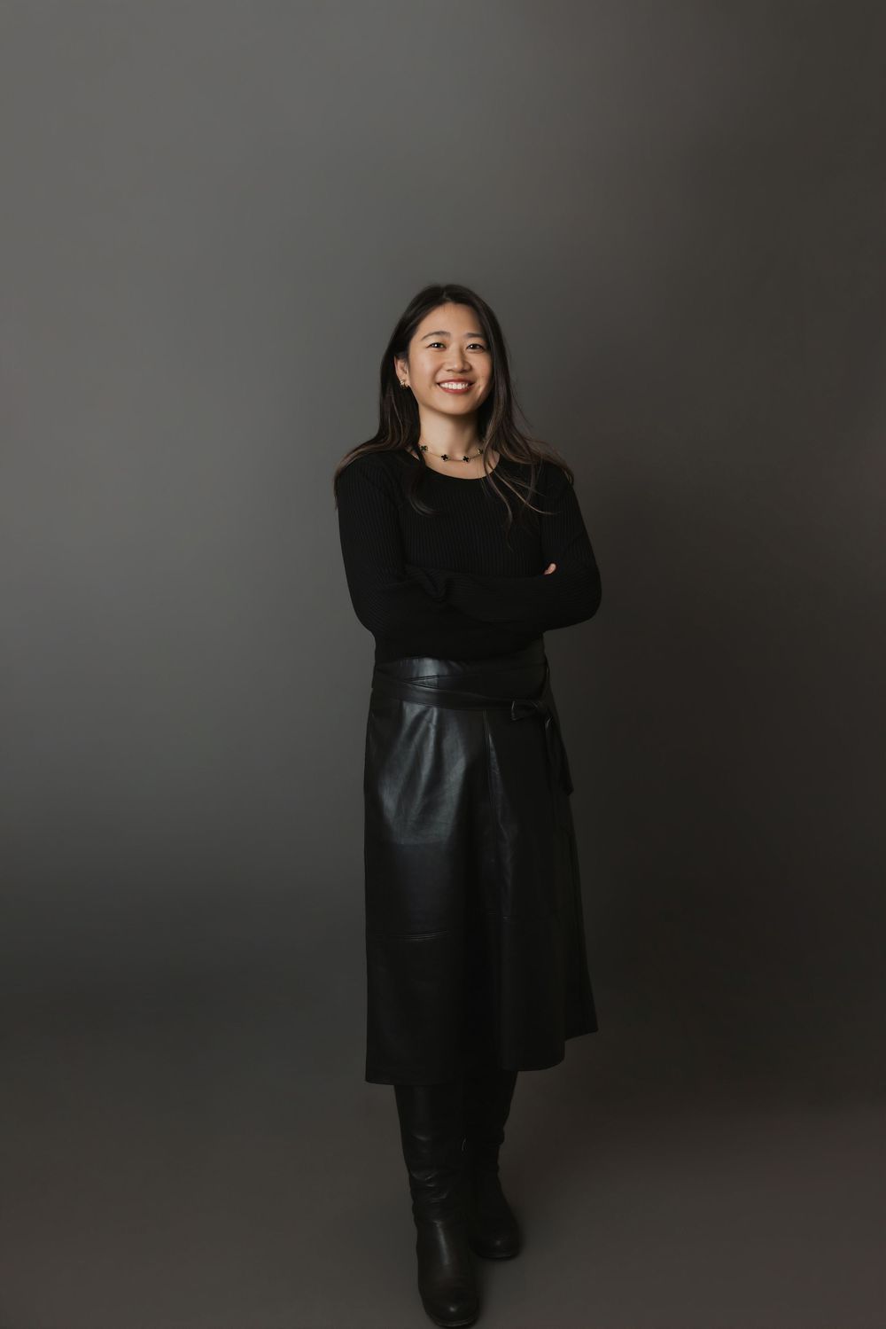 A figure in all black attire poses dynamically against a dark gray studio backdrop in a fashion editorial style series.