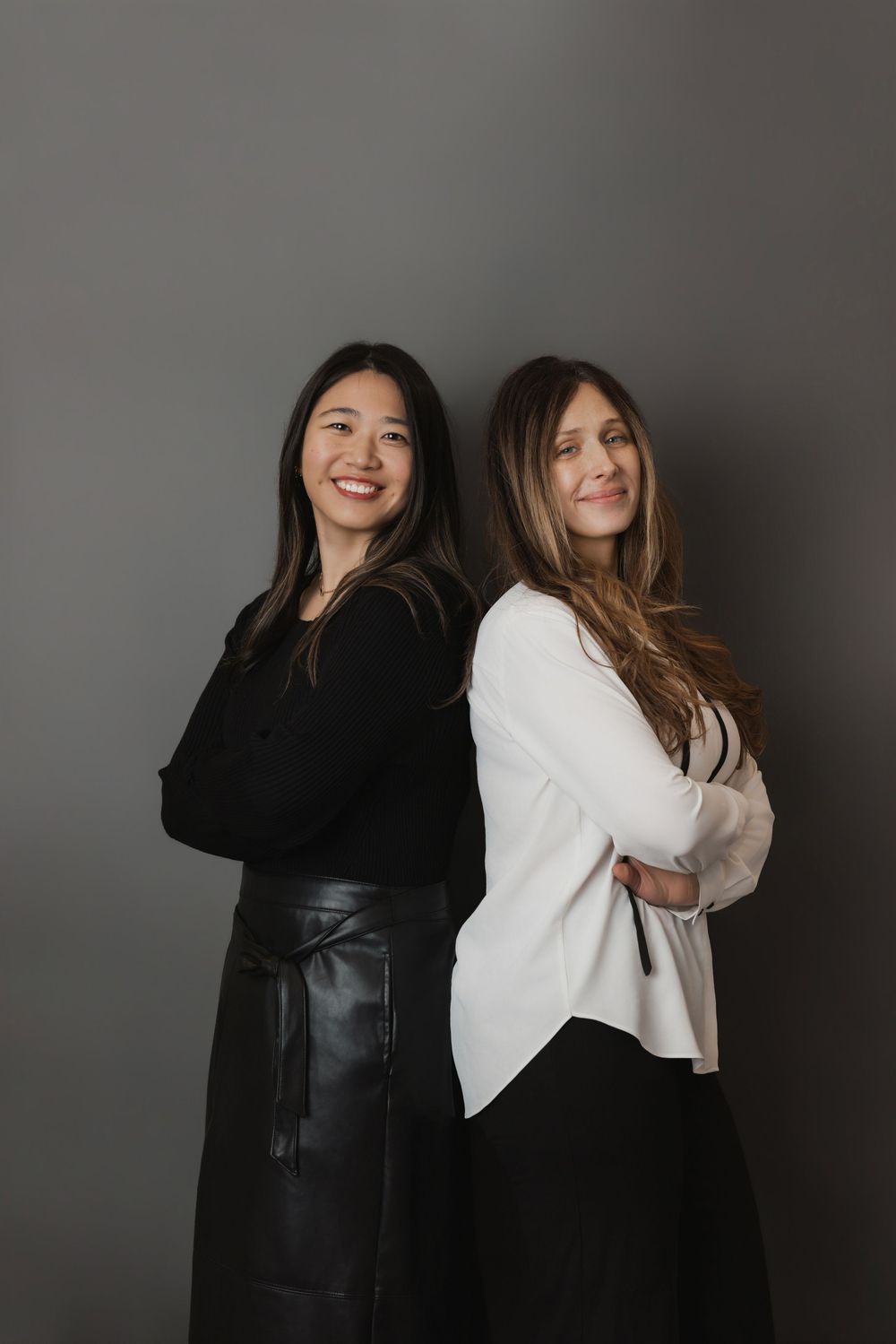 Two friends in contrasting black and white outfits pose playfully against a gray studio backdrop.