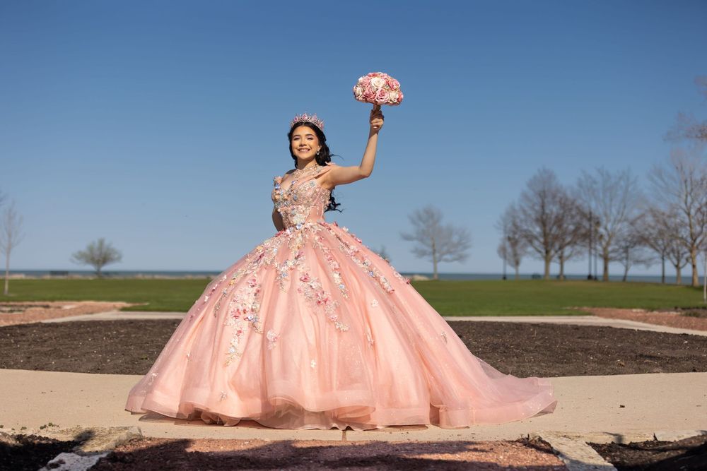 Quinceañera cheering with her bouquet against a blue sky. Joyful Mis XV portraits in Lake County, IL by Alex T Photography.