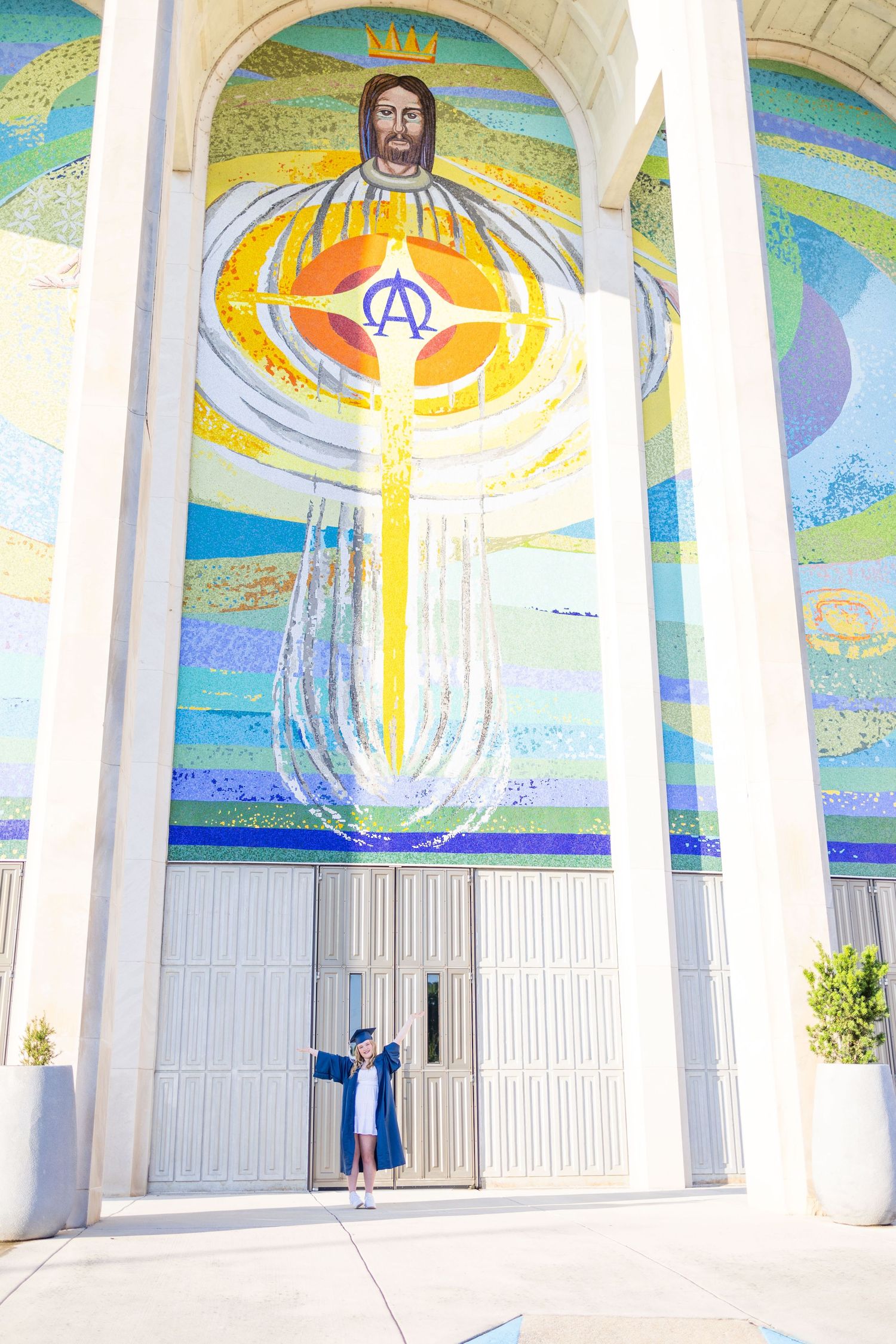High school senior in front of "egg beater Jesus" church in graduation cap/gown.