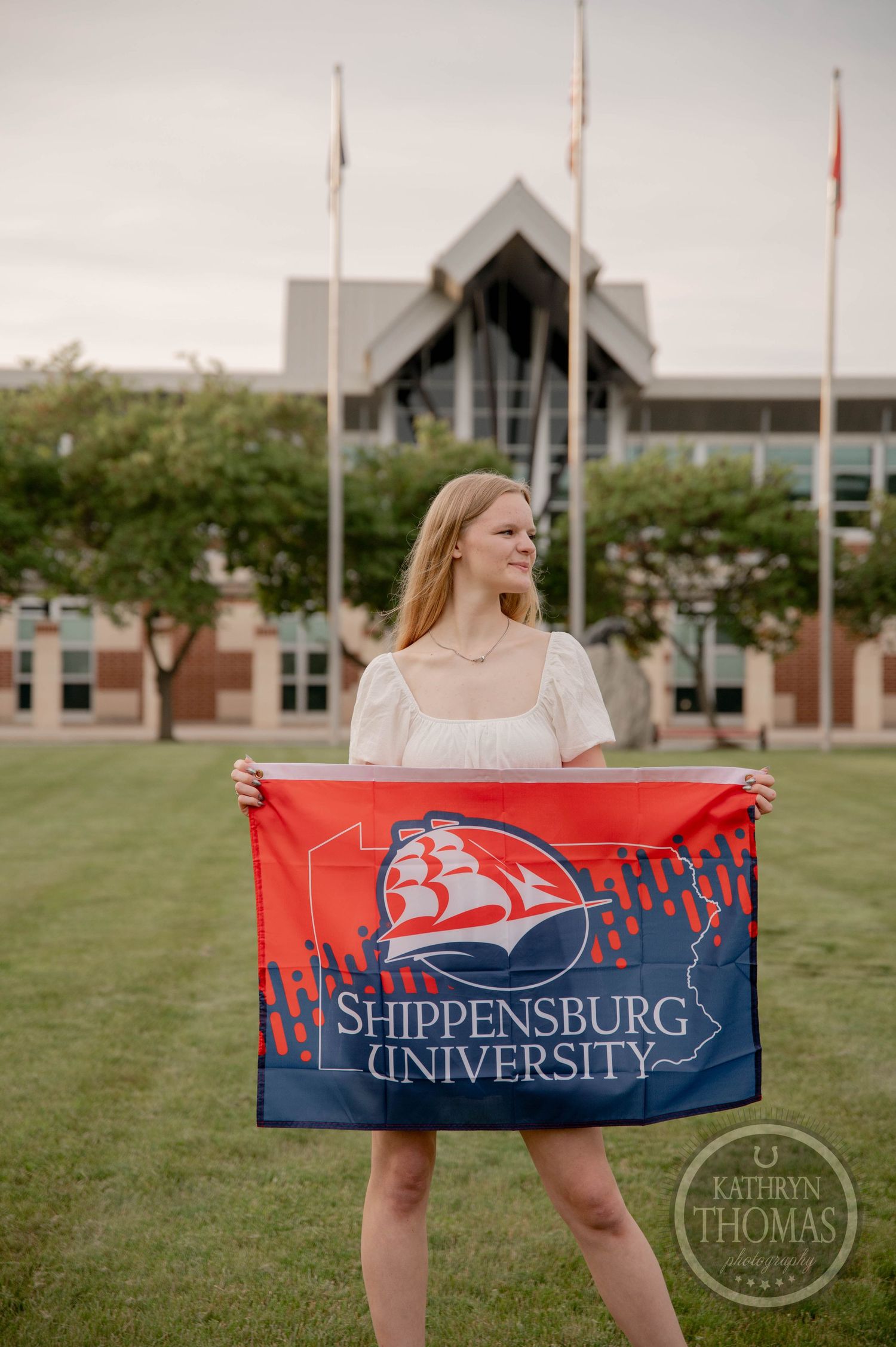 A student displays a red and blue Shippensburg University banner flag while standing on campus grounds.