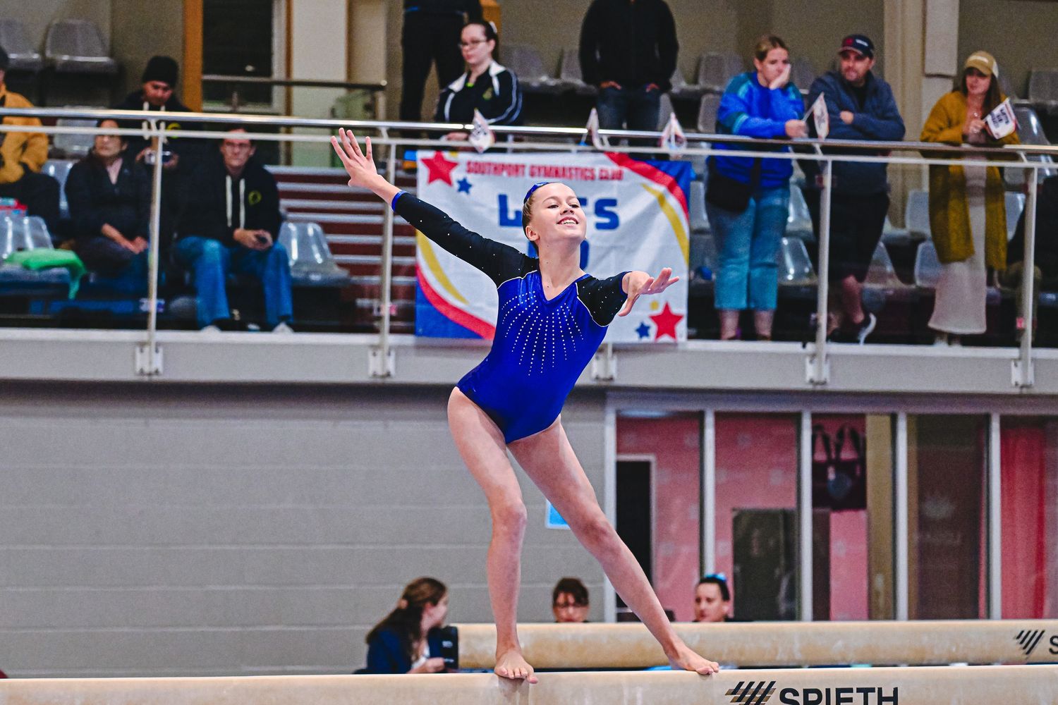 A gymnast performs a skilled split handstand on the uneven bars during a competition routine.