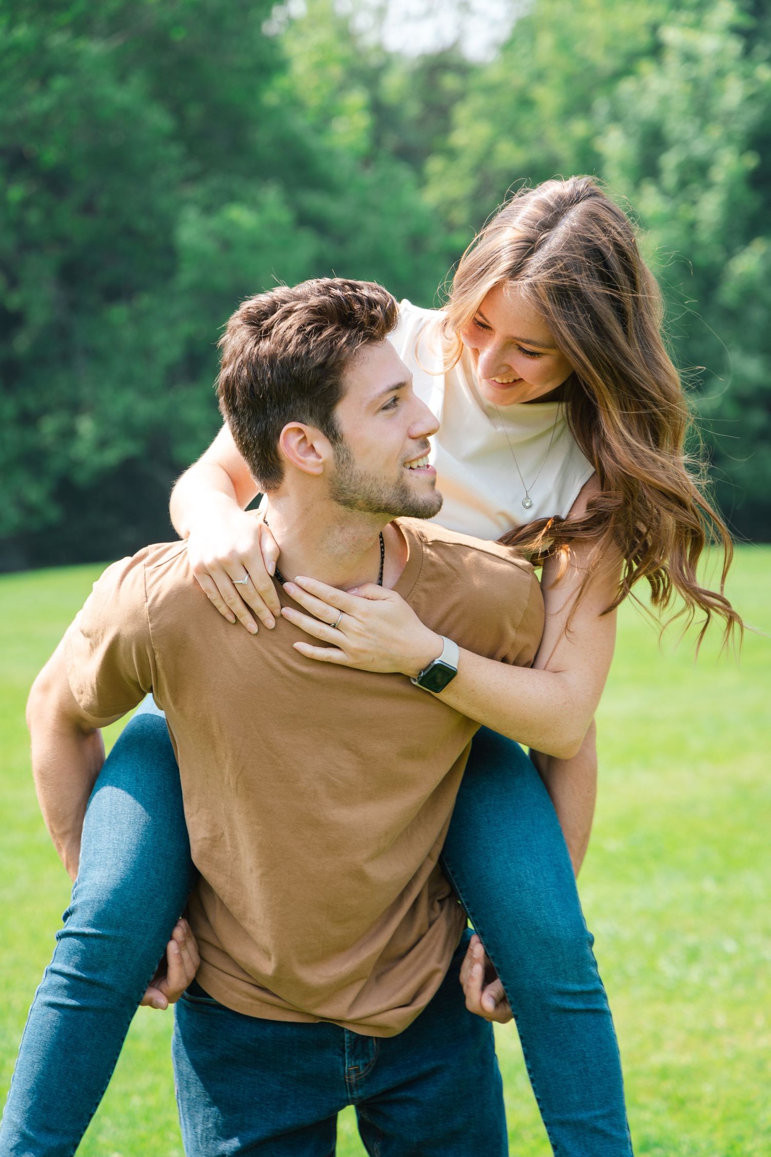 A joyful couple sharing a playful piggyback ride moment in a sunny green park setting.