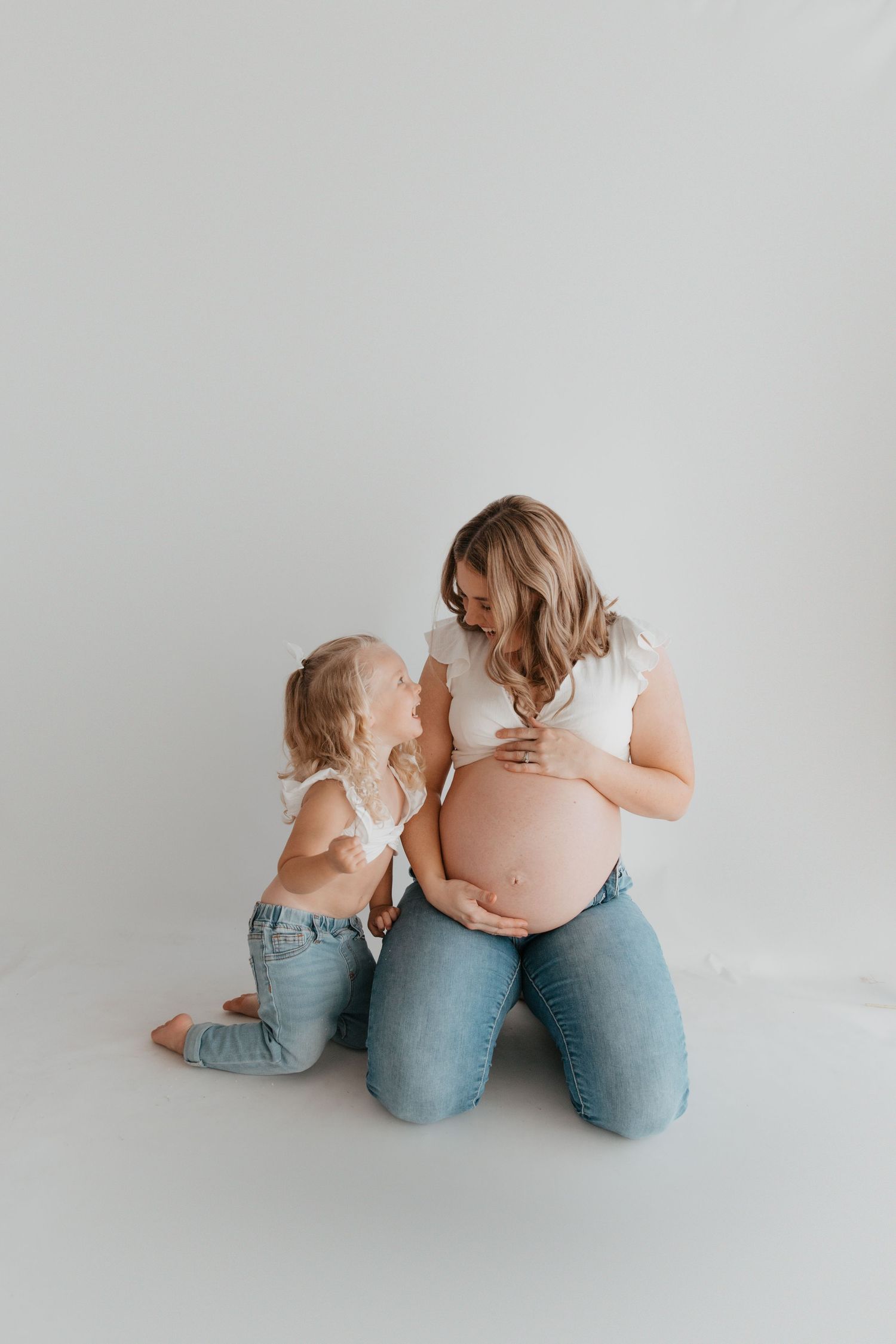 Matching mother and child sitting together in casual denim against white background.