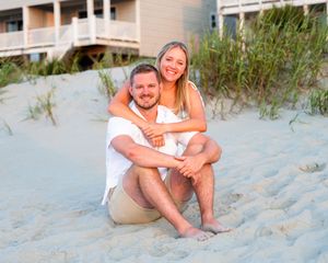 Happy couple embracing and smiling while sitting together on a sandy beach during golden hour.