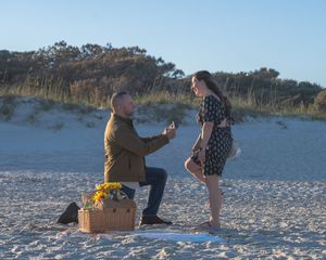 A couple shares a special moment during a romantic beach proposal with yellow flowers at sunset.