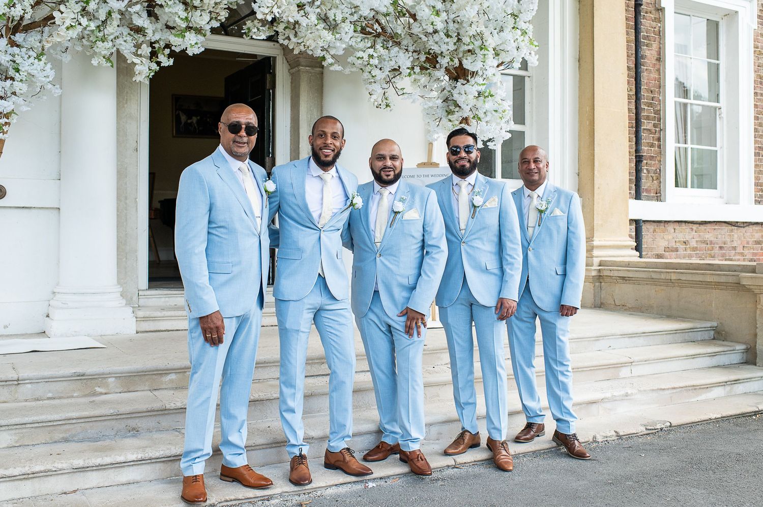 Five gents in pale blue suits stand in front of wedding entrance