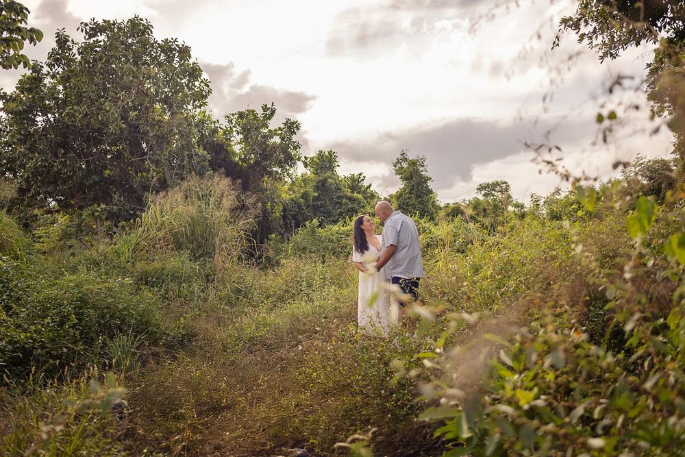 Couple walking through lush green coastal vegetation path during golden hour.
