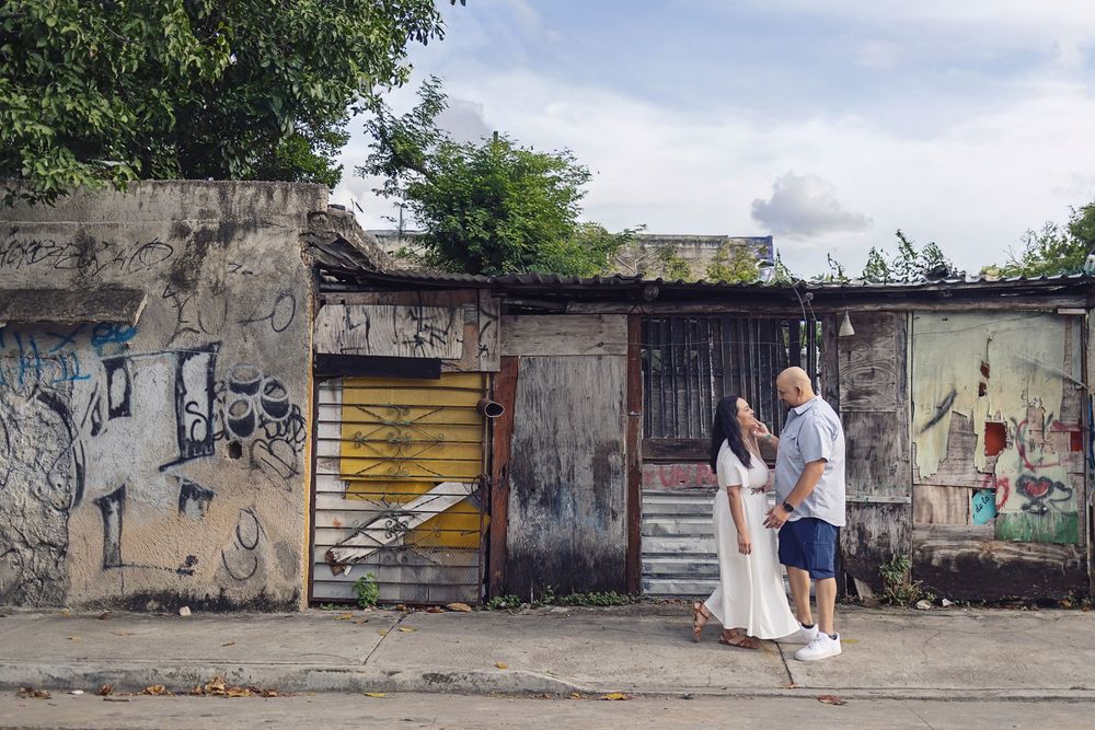 A couple poses against a graffitied concrete wall with metal doors in an urban setting.