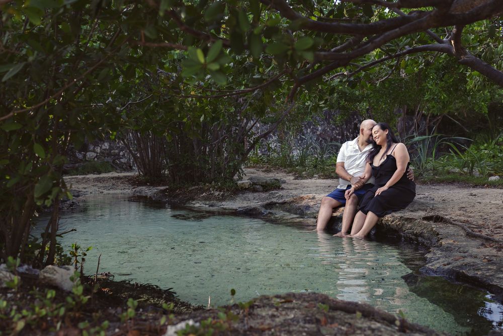 People enjoying engagement photos in front of a creek amid lush greenery.