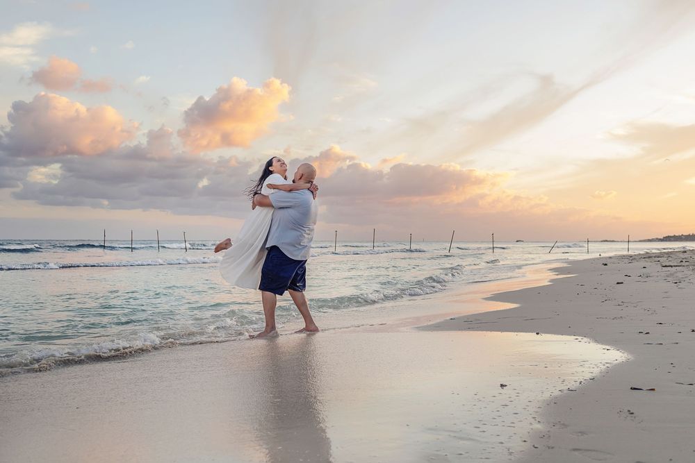 Romantic couple walking along tropical beach at sunset with waves lapping at sandy shore.
