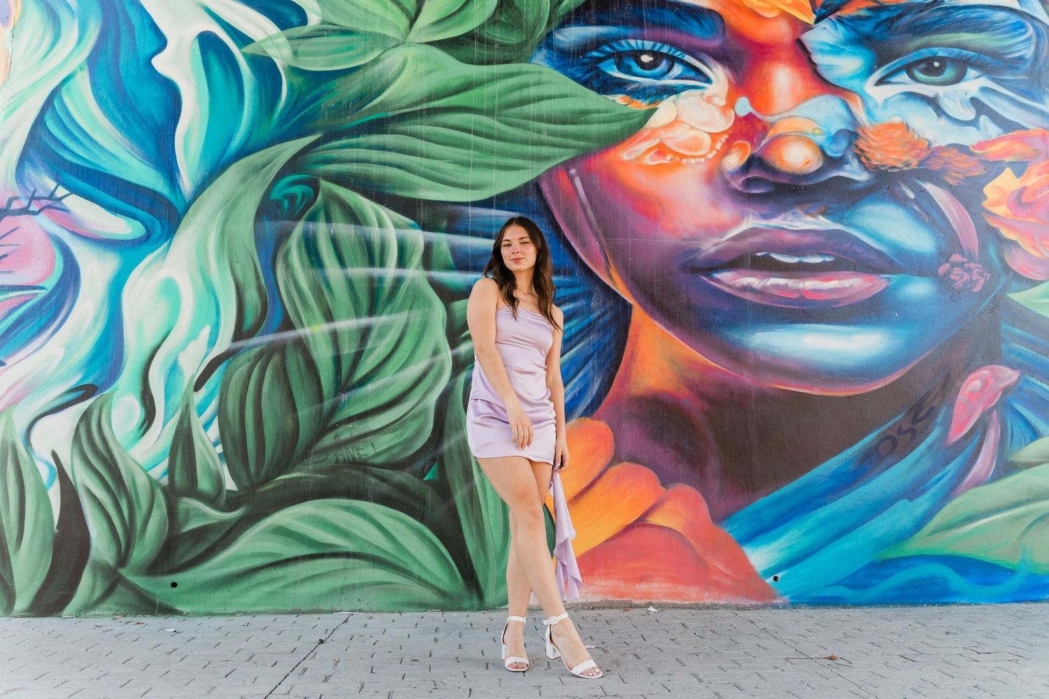 A Perrysburg High School senior in purple dress stands against a vibrant graffiti street art mural featuring colorful artwork during session