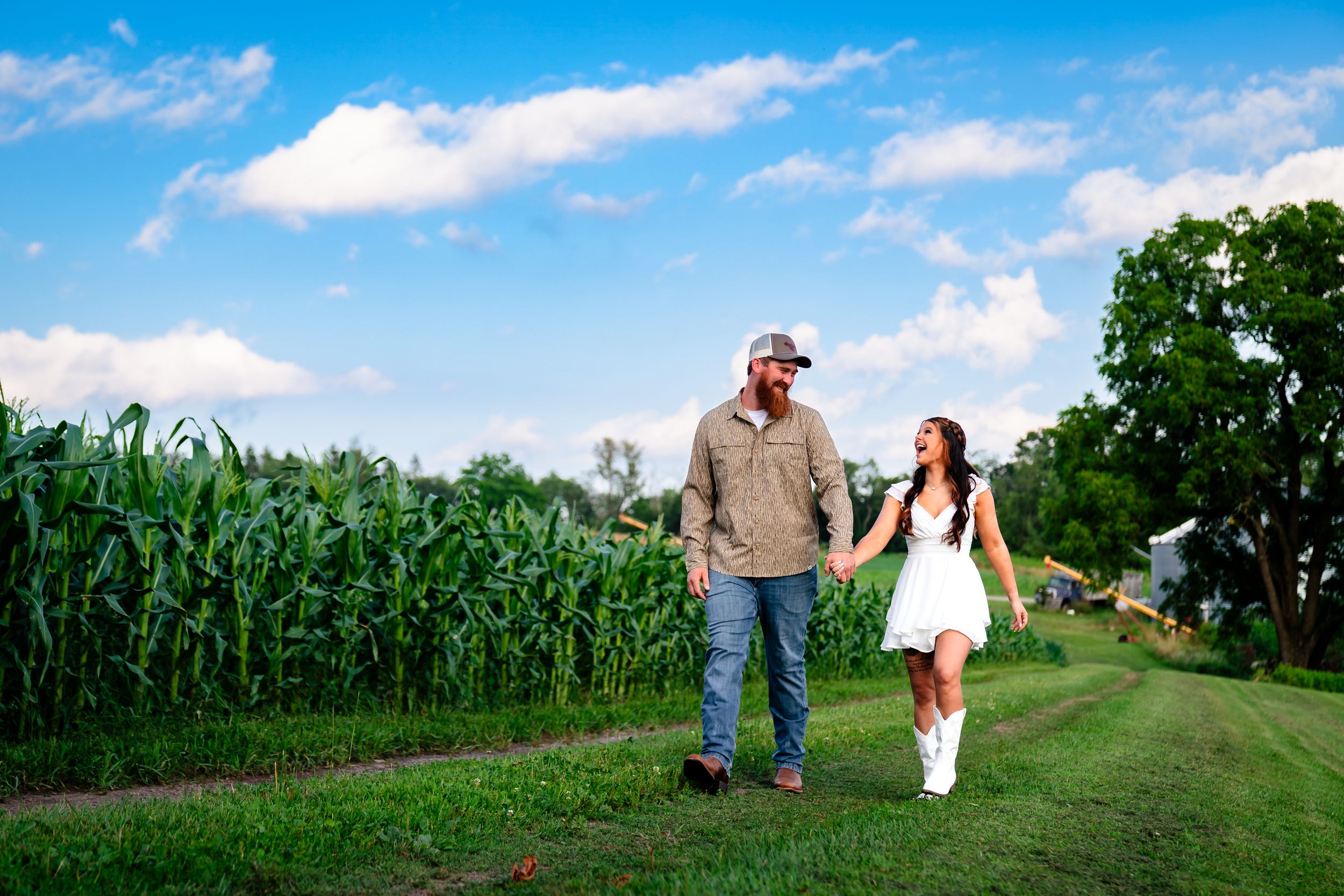 A panoramic view of a couple walking along a country path between cornfields on a sunny day.