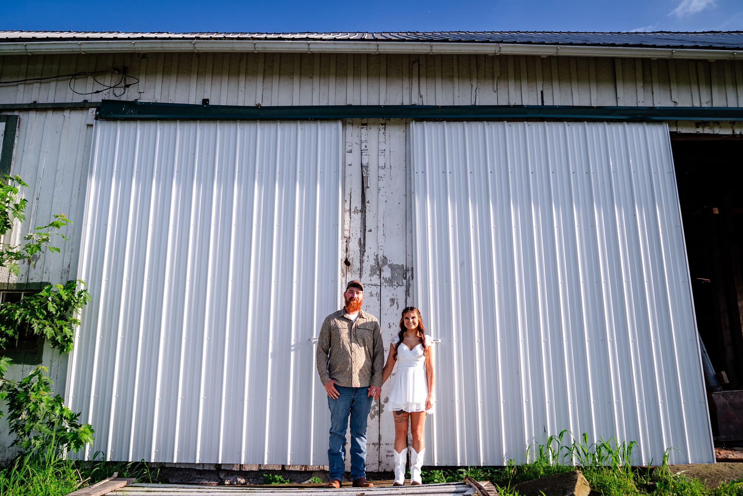 A rustic metal barn exterior with white paneling against a bright blue sky.