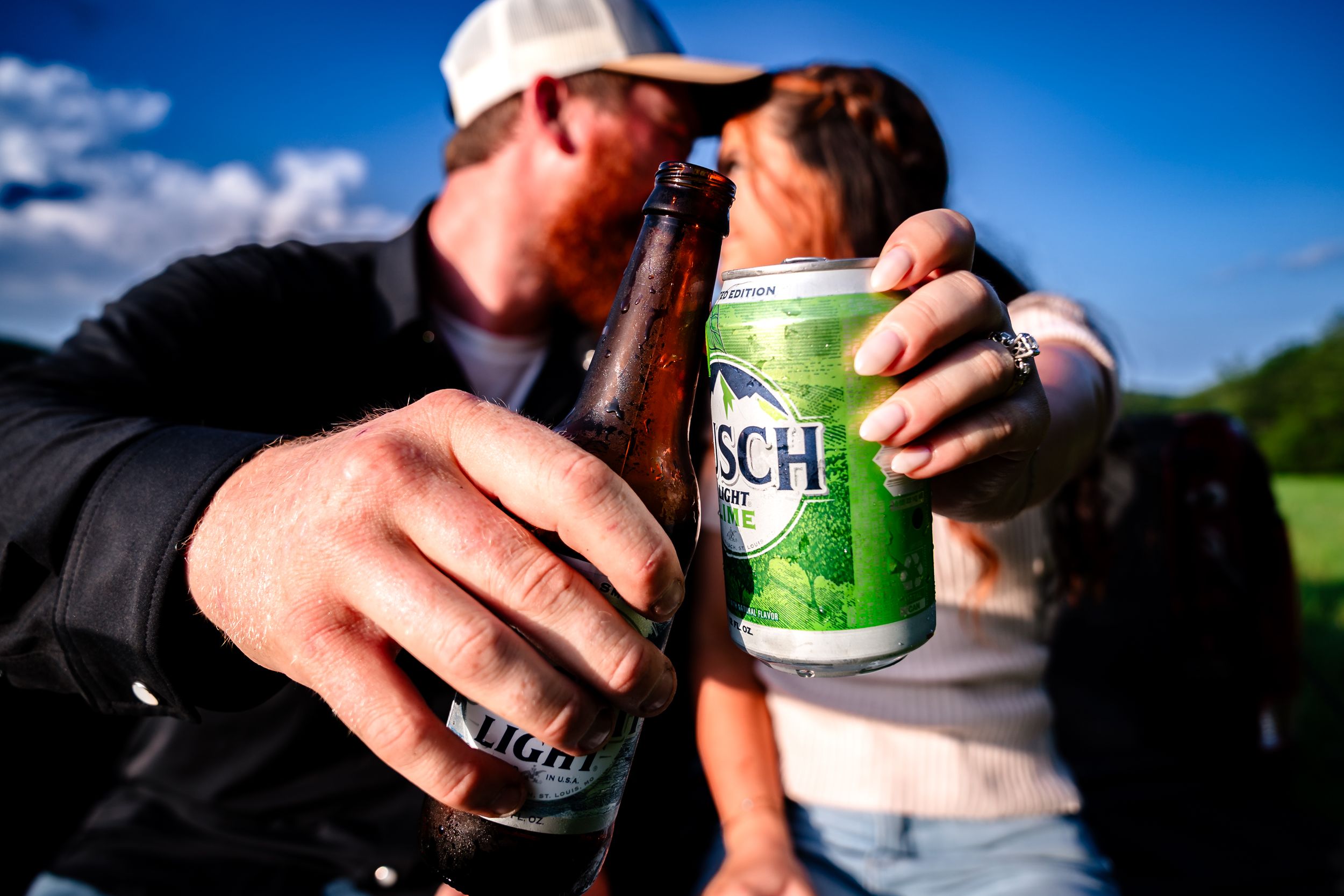 Close-up of hands holding beer cans during outdoor celebration.