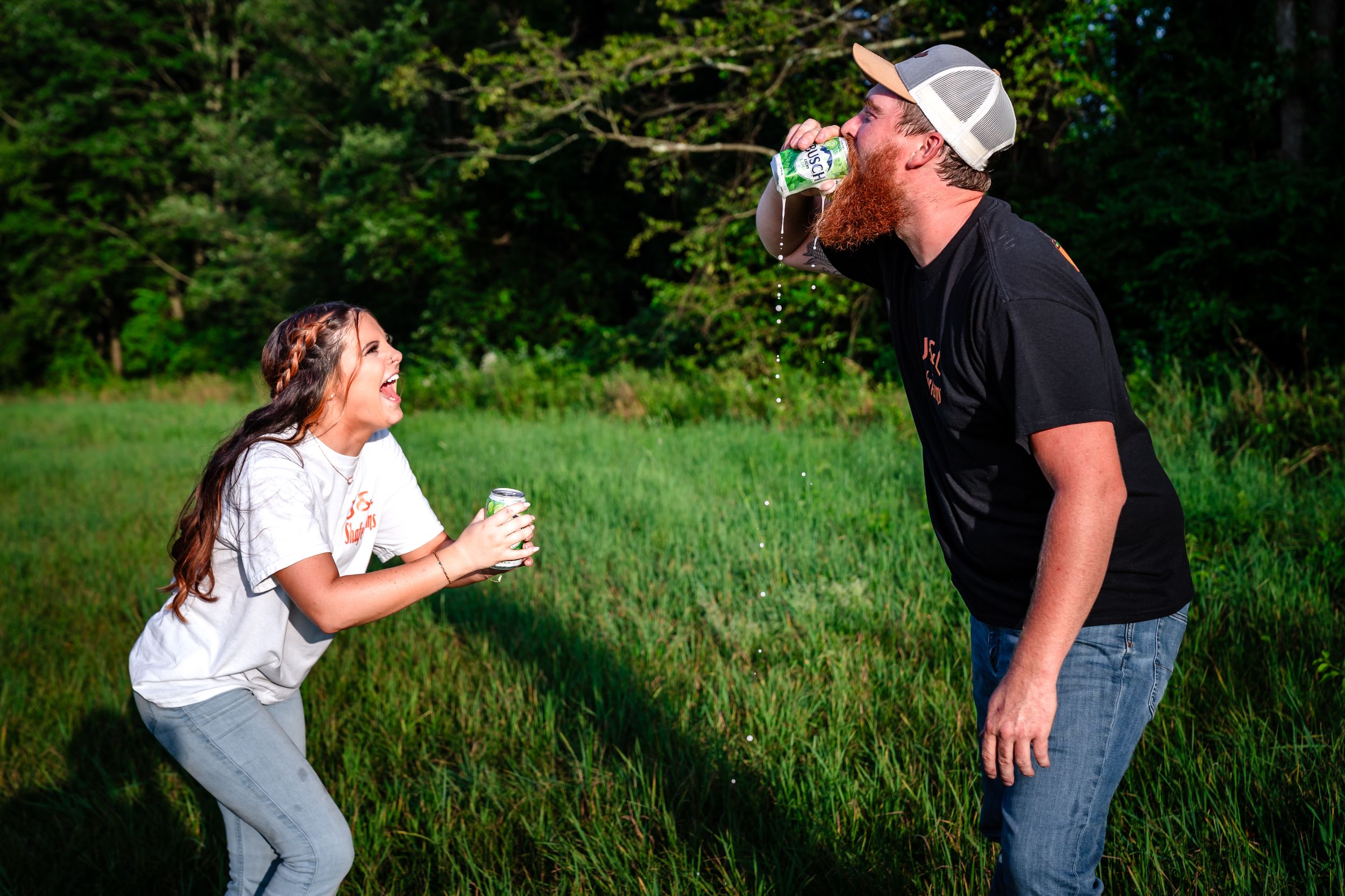 Playful engagement photos taken in a lush green field during golden hour.