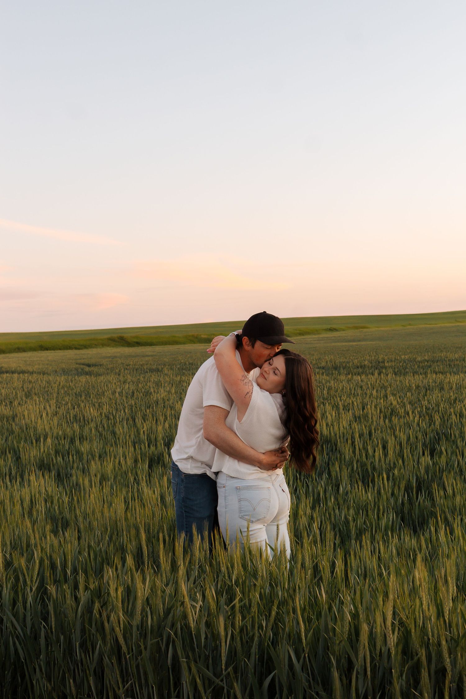 Couple hugging in wheat field in Montana. There is a pink and golden sky.