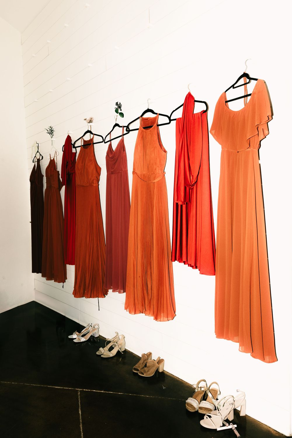 A row of orange and red bridesmaid dresses hanging with shoes lined up underneath.