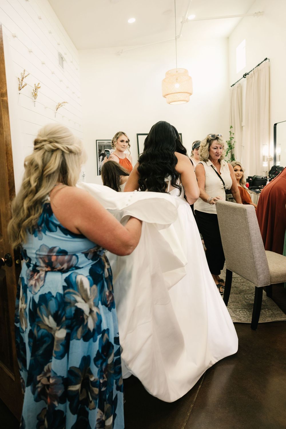 Wedding dress preparation with attendants helping in a bridal suite.