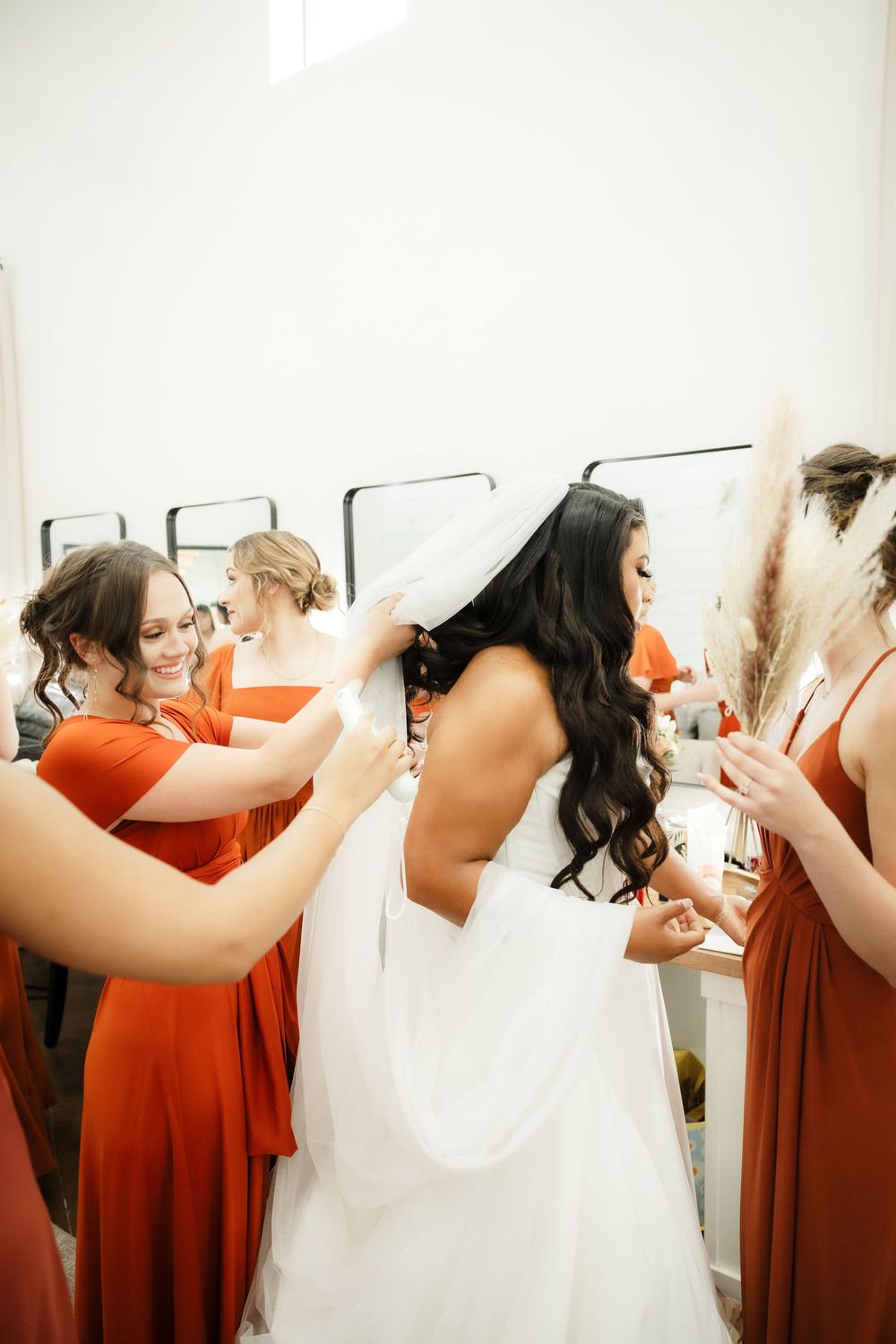 Bridesmaids in coral dresses help adjust a wedding gown during pre-ceremony preparations.