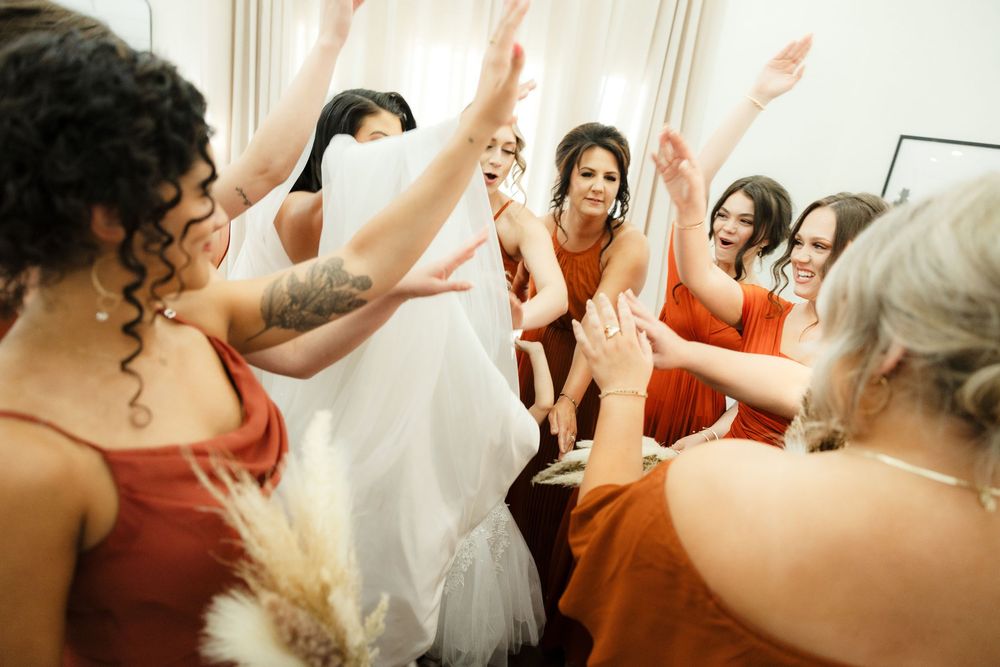Wedding party celebrating joyfully with raised hands in a bridal suite.