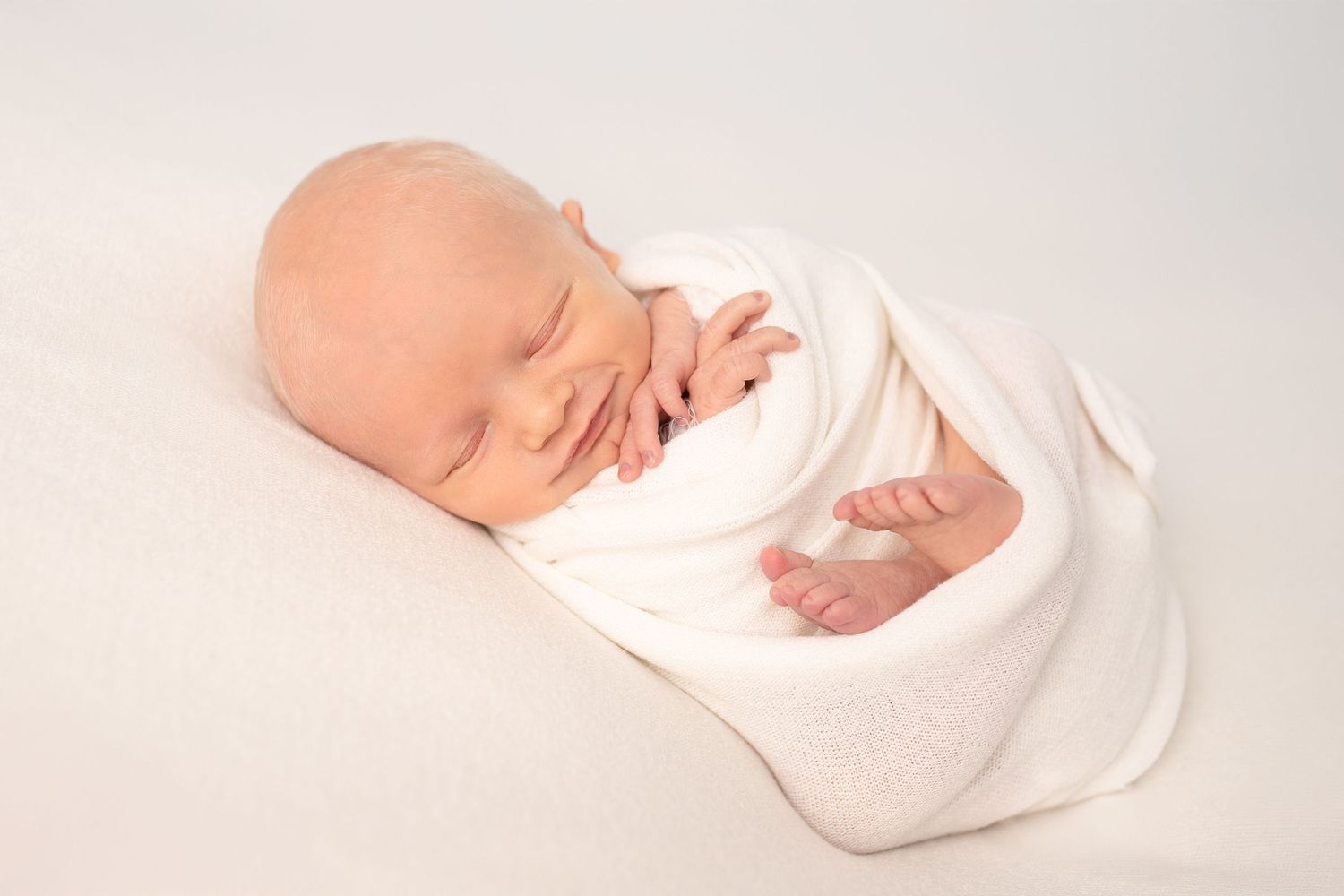 A newborn baby sleeping peacefully on soft white blankets in a collection of tender moments captured in natural light.