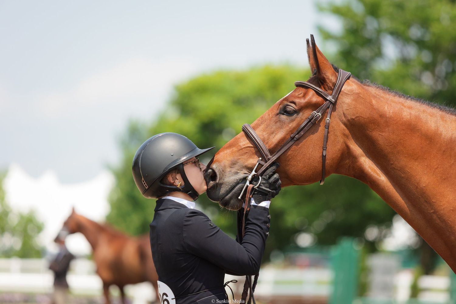 Equestrian in black helmet and jacket shares tender moment with chestnut horse during practice session outdoors.