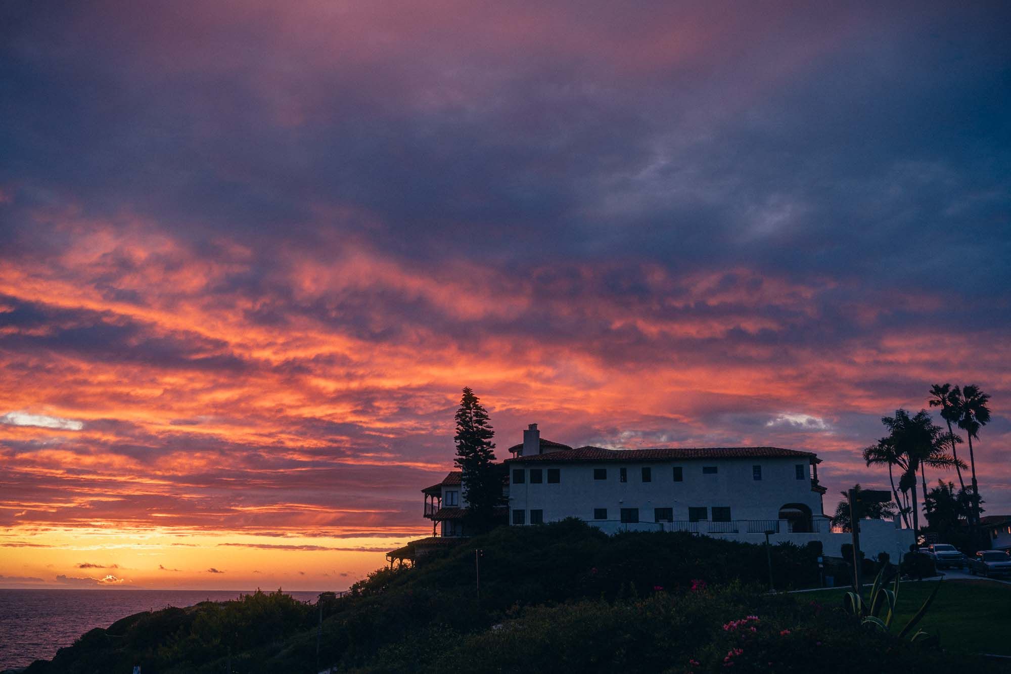 Stunning wide-angle sunset view of a coastal property with dramatic red and purple clouds over the ocean.
