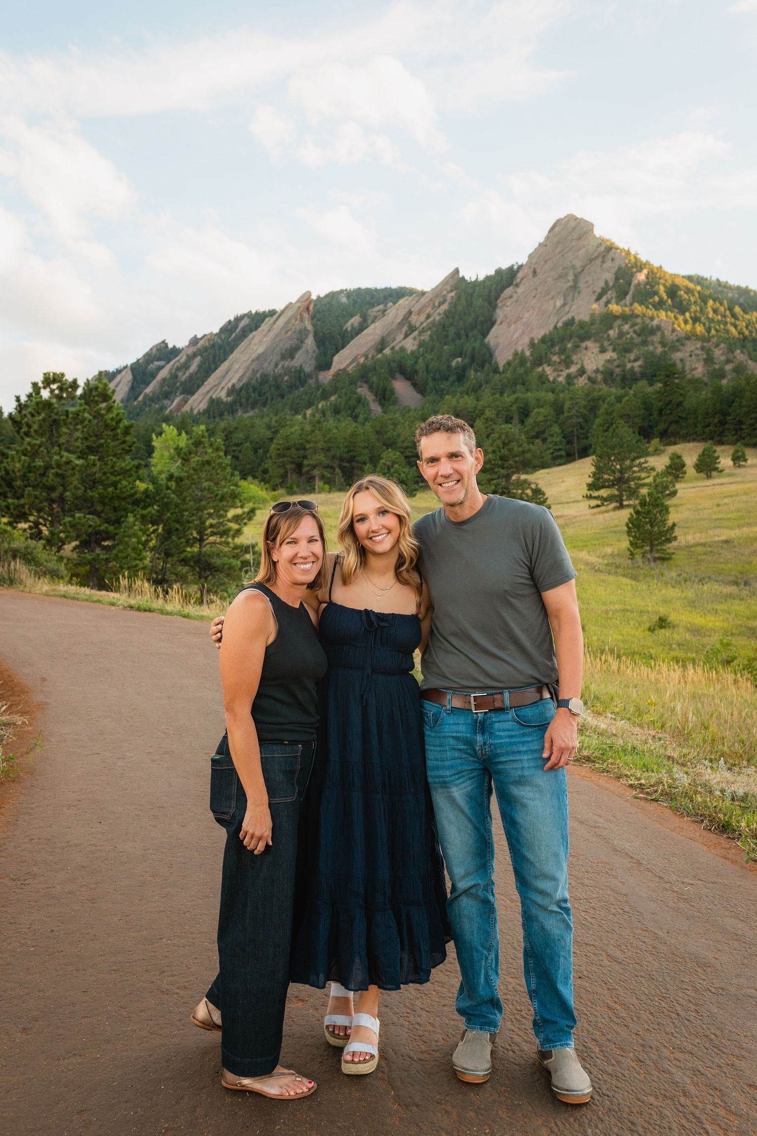 Three people pose on a path with the iconic Flatirons rock formation in Boulder, Colorado in the background.