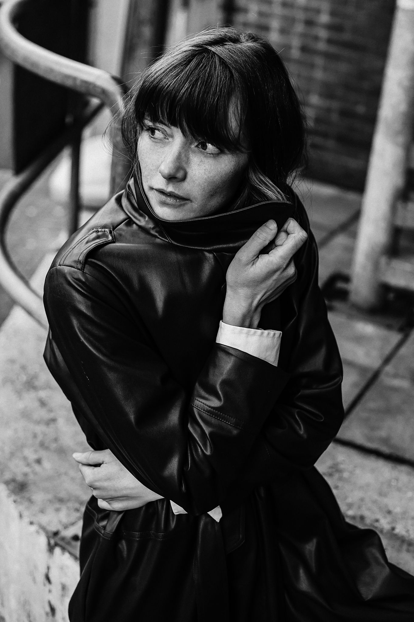 A contemplative person sits in tall grass wearing a dark jacket and white shirt during an outdoor portrait session.
