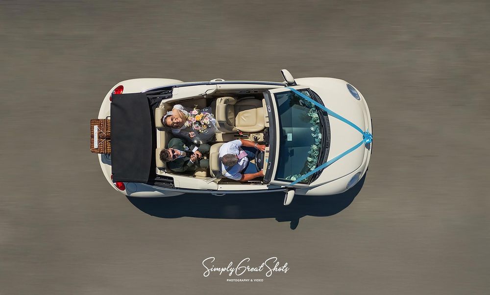 Beaumanor wedding photographer captures the married couple from above, smiling with champagne in hand in a convertible VW beetle.